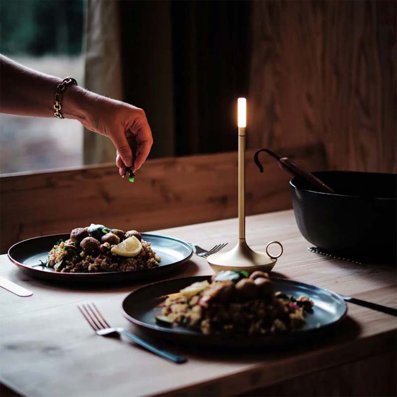 Two plates of food on a table with a candle and a person's hand reaching for something.