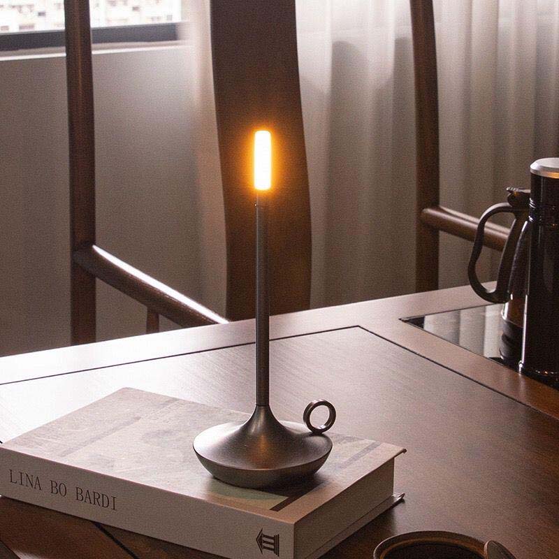 Modern table lamp with a warm glow on a book, set against a blurred indoor background.