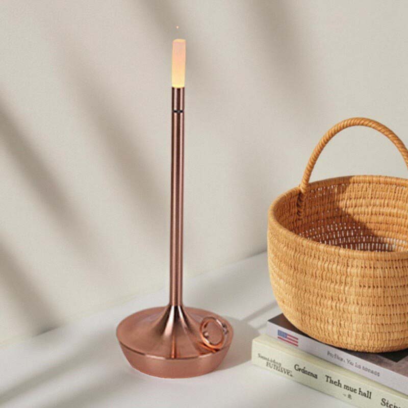Copper candle holder with a lit candle on a surface next to a woven basket and books.