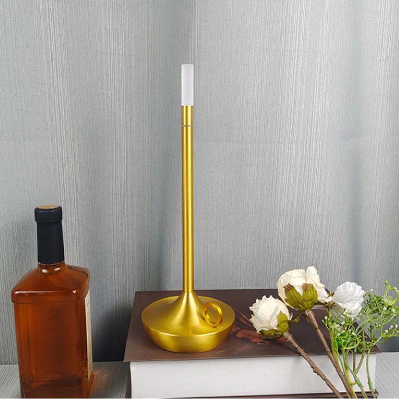 Gold candle holder with white candle on a wooden surface against a gray wall.