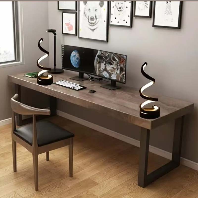 A modern computer desk setup in a home office environment, featuring a long gray wood-grain desk with a black metal leg base, a matching wooden chair with a black seat, dual spiral-shaped black desk lamps, a computer monitor, and a keyboard.