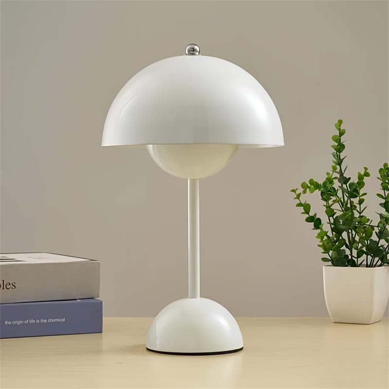White table lamp on a wooden surface with books and a plant in the background