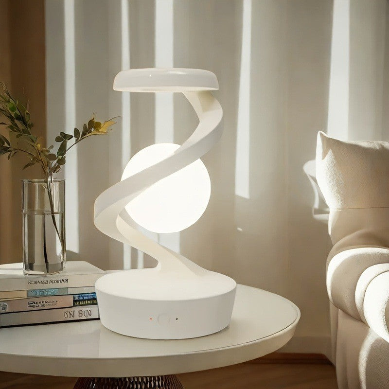 Saturn Helix – LED Desk Lamp with Wireless Charging on a round white table with books and a plant in the background.