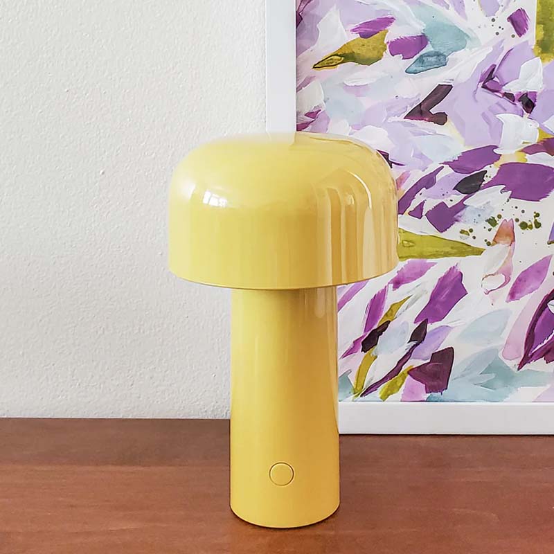 Rechargeable Mushroom LED Table Lamp sits on a wooden surface against a white wall and colorful abstract art print.